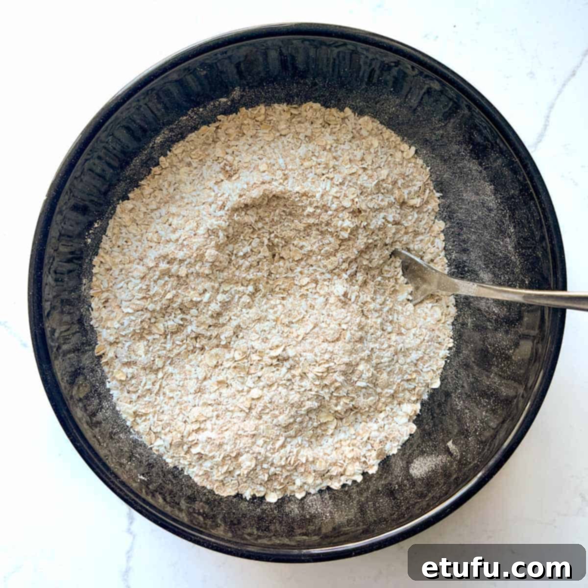 Mixed dry ingredients for the coconut biscuits in a large black bowl.