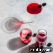 Blackberry simple syrup in a carafe next to a glass of blackberry syrup with lemonade and a blackberry martini.