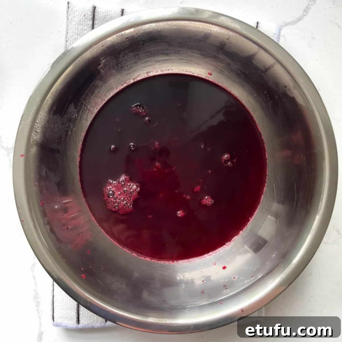 Strained blackberry simple syrup in a stainless steel bowl.