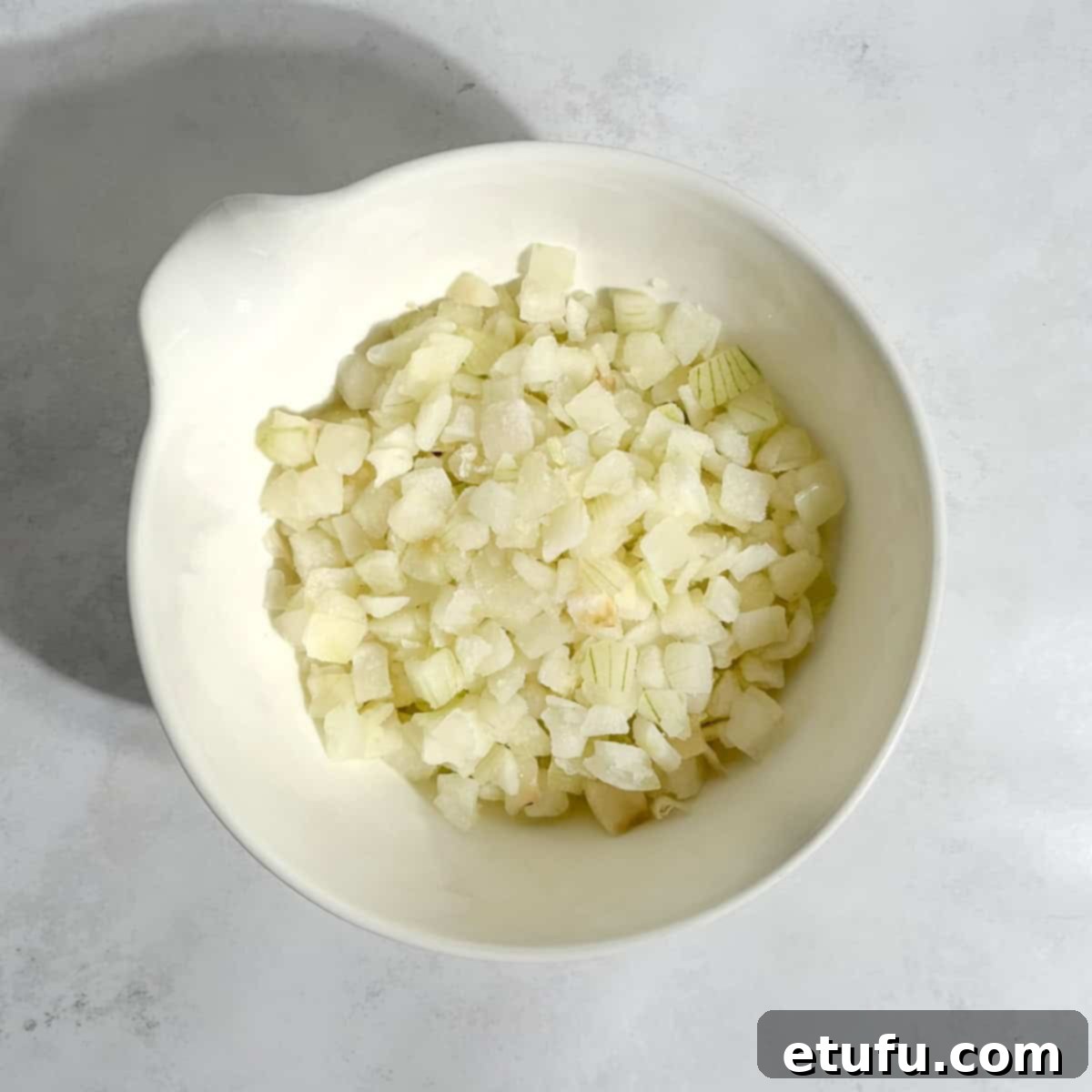 Finely diced onion, neatly presented in a small white bowl, prepared for the Chicken Pasanda.