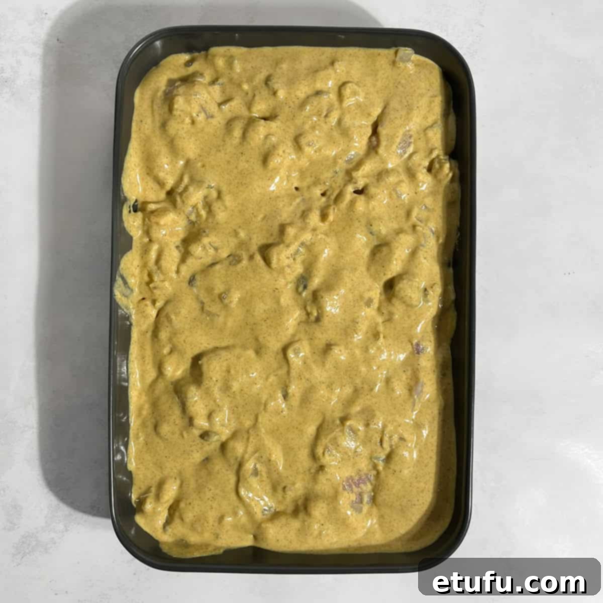 The rich Pasanda sauce being poured generously over chicken and onions in a black baking dish, ready for the oven.