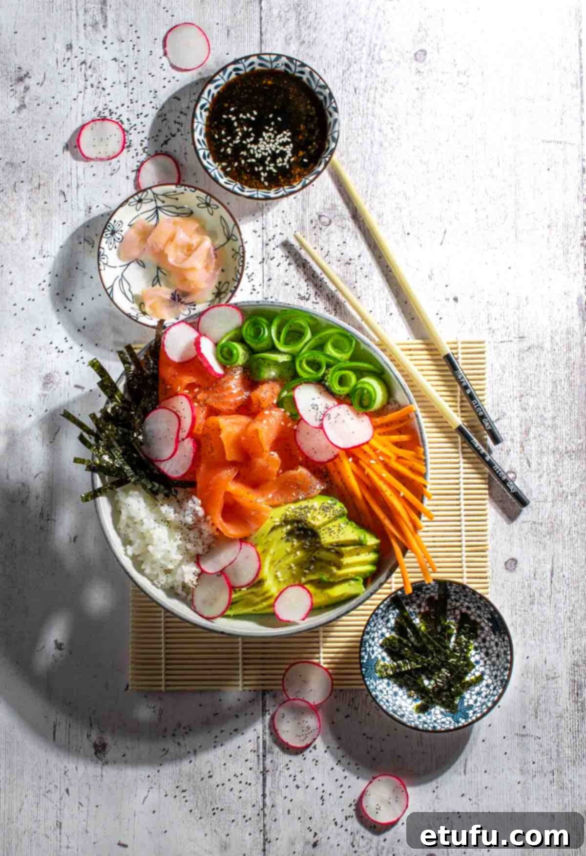 Sushi salad in a white bowl with extra bowl of ginger, salad dressing and nori strips.