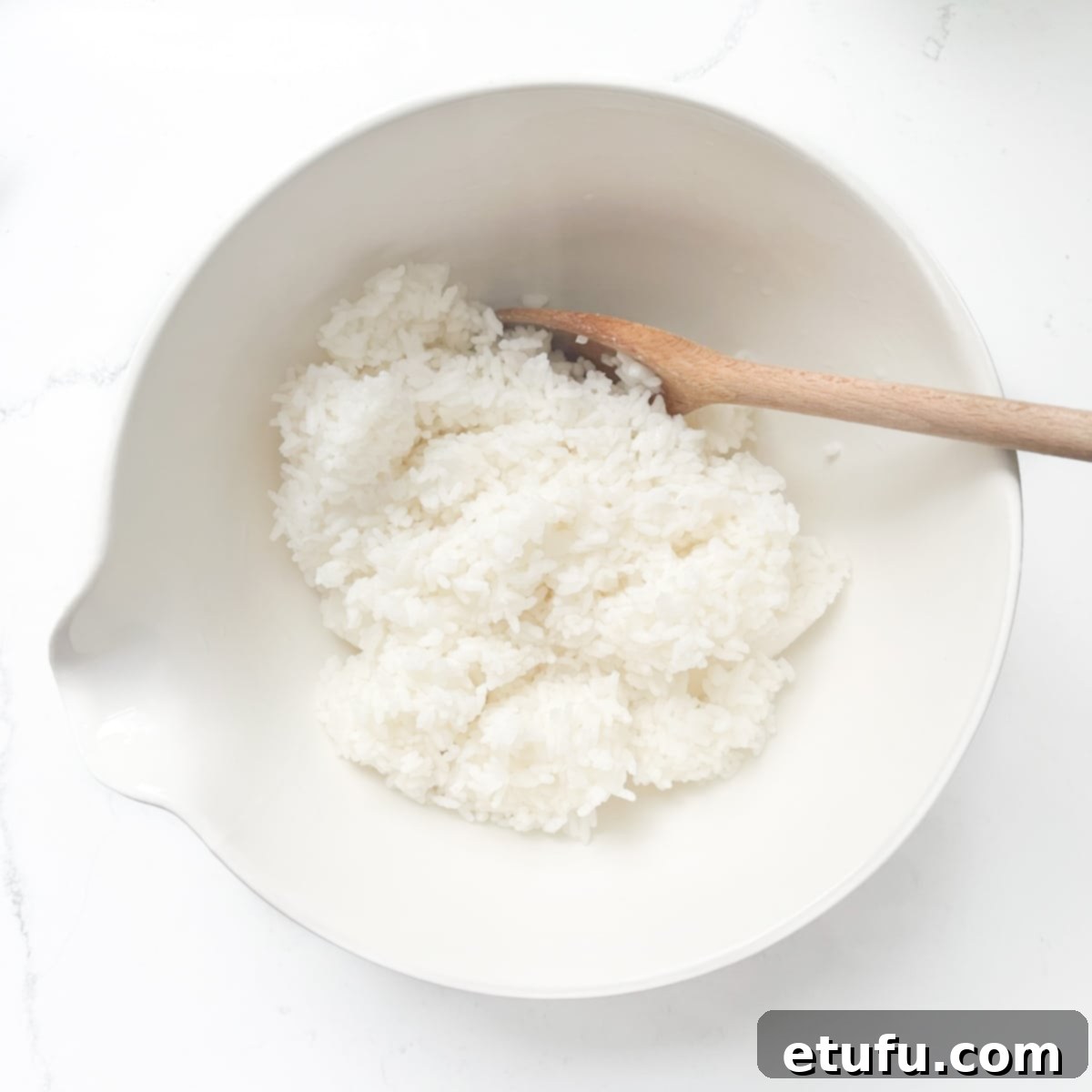 Cooked sushi rice in a bowl with a wooden spoon.