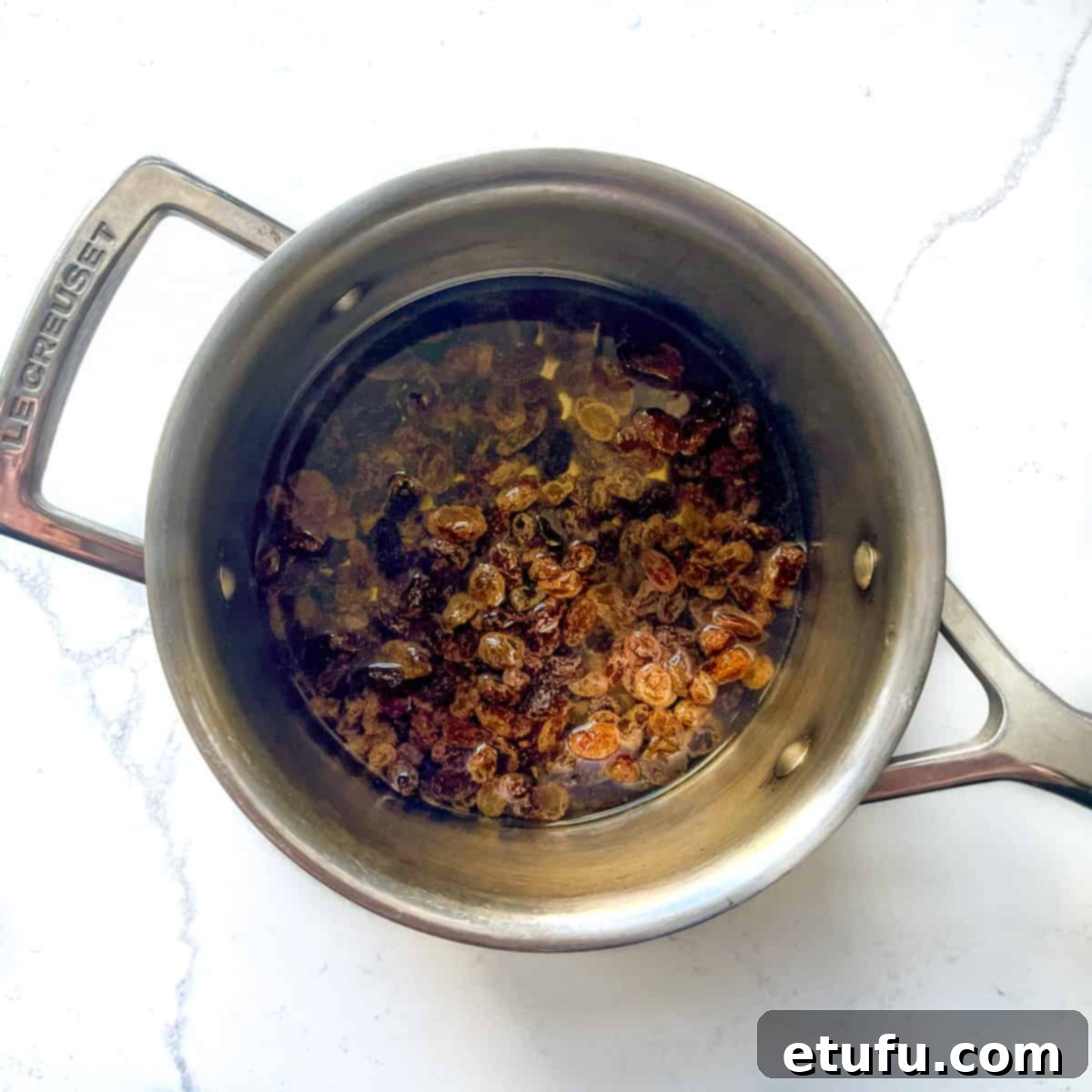 Sultanas submerged in water in a small saucepan, ready for pre-cooking to plump them up.
