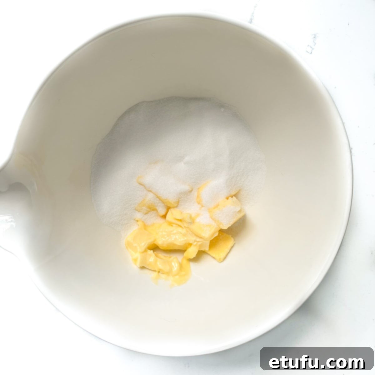 Softened butter and caster sugar combined in a large white mixing bowl, ready to be creamed together.