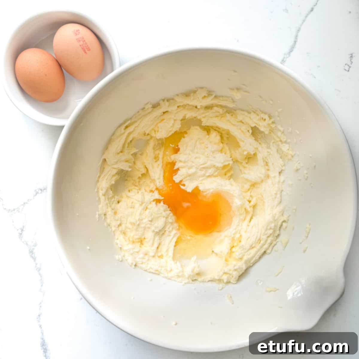 A cracked egg being added to the creamed butter and sugar mixture in a large bowl, ready for mixing.