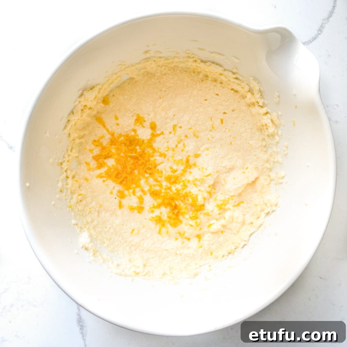 Fresh lemon zest being sprinkled into the cake mixture, adding a bright citrus aroma.