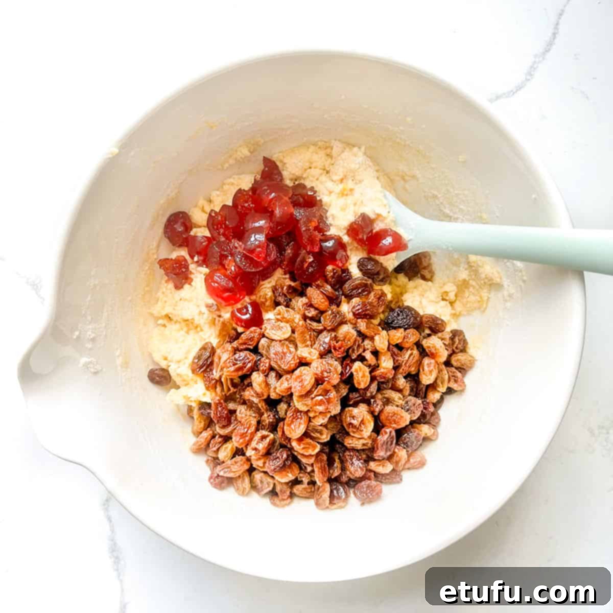 Plump sultanas and quartered glace cherries added to the cake batter, ready for a final gentle fold.