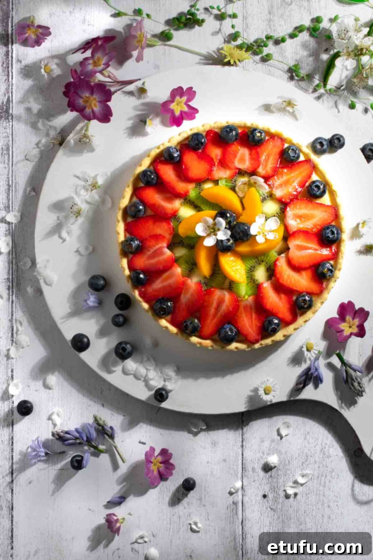 Exquisite French Fruit Tart 2 Tarte aux Fruits on a white board, surrounded by flowers.