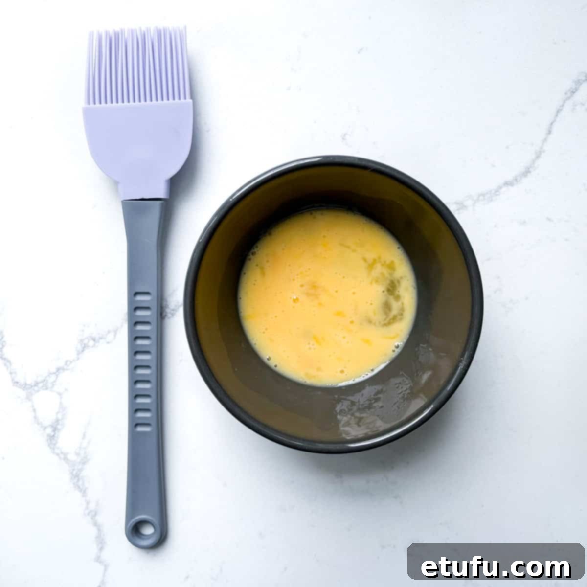 Exquisite French Fruit Tart 23 Egg wash in a small bowl with a pastry brush to the side.