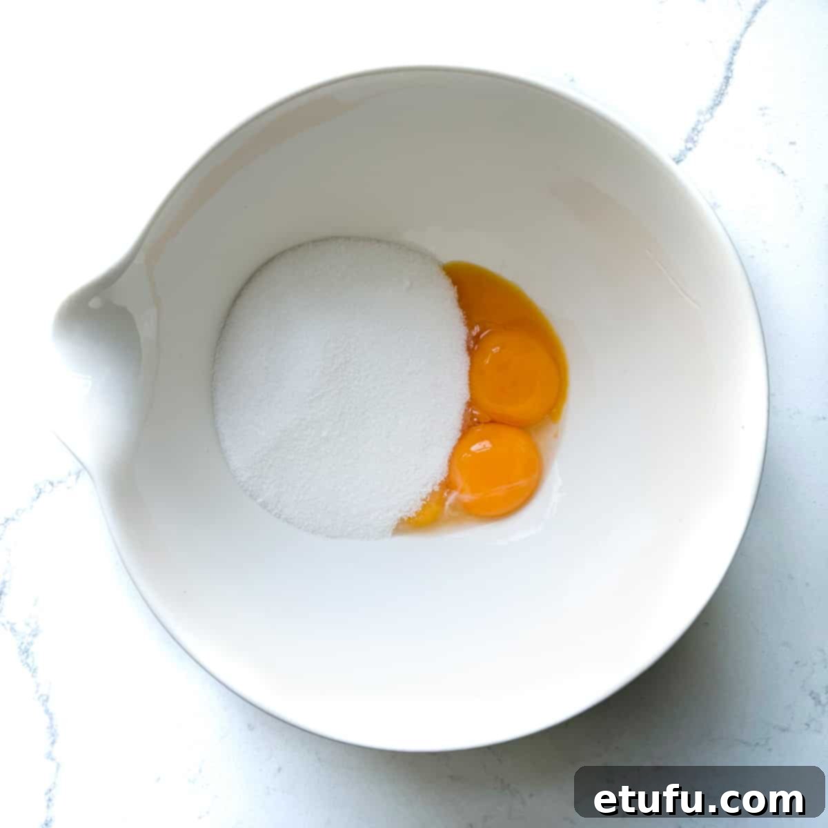 Exquisite French Fruit Tart 25 Adding sugar and eggs to a small white bowl.