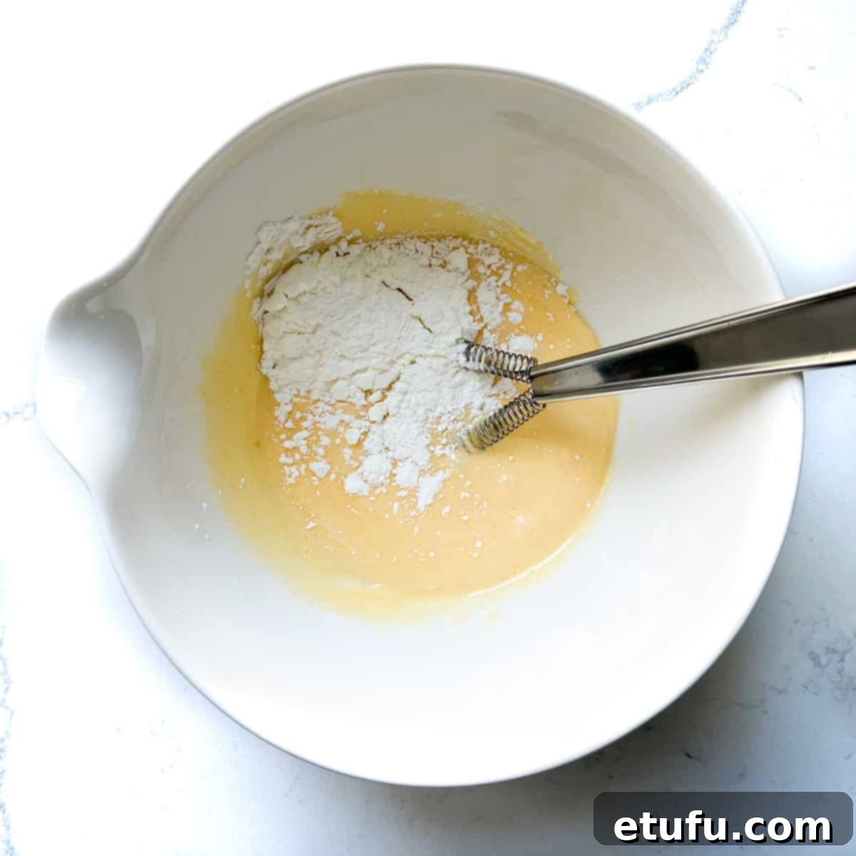 Exquisite French Fruit Tart 27 Adding cornflour to egg yolks and sugar in a white mixing bowl.