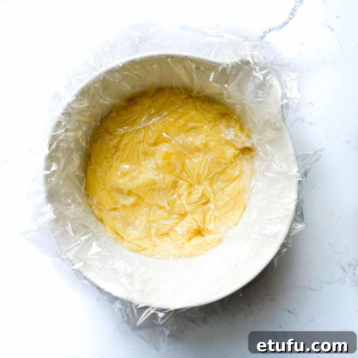 Exquisite French Fruit Tart 37 Plastic wrapped draped onto the top of the creme pattisiere in a white bowl.