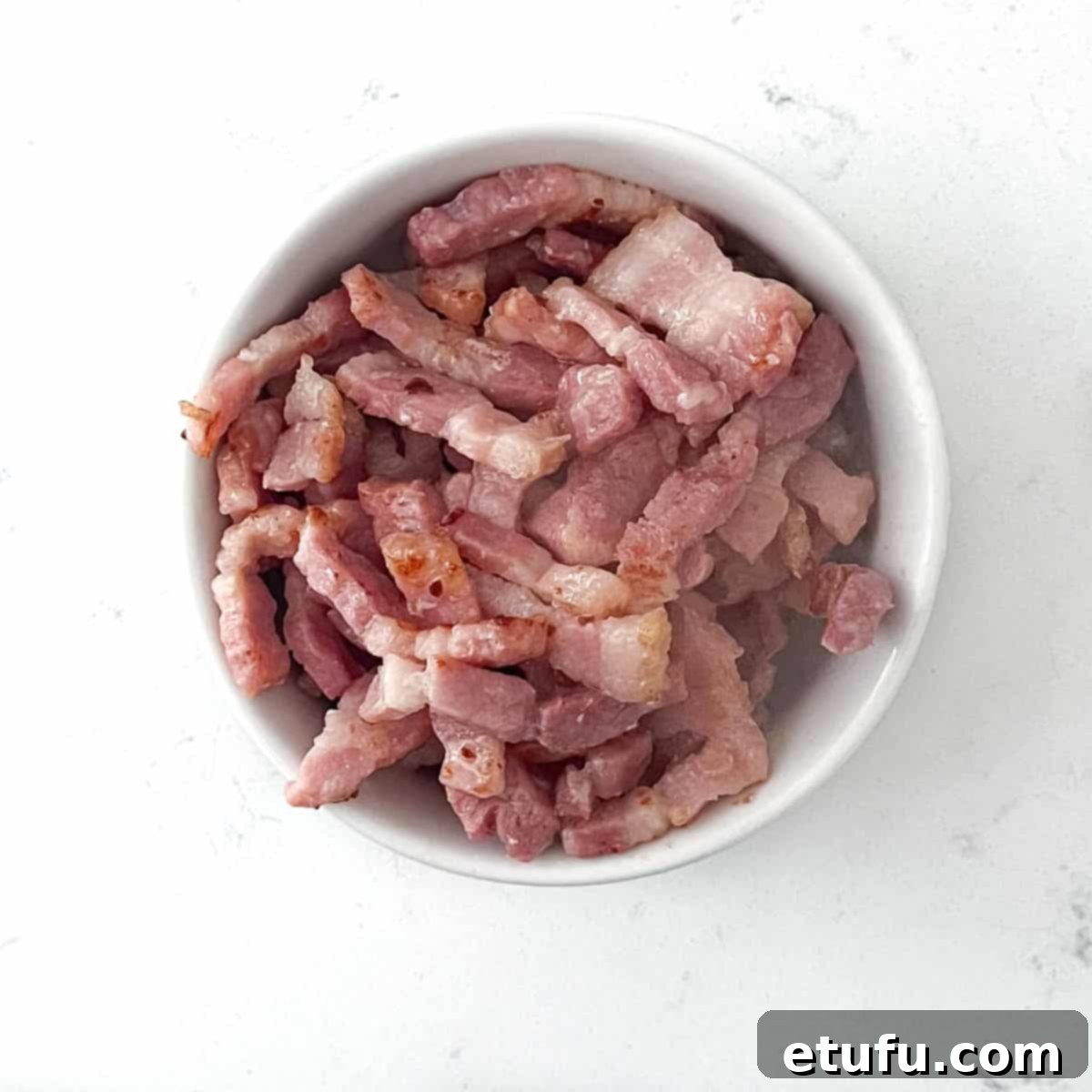 Crispy, golden-brown fried bacon lardons served in a small white ceramic bowl, ready to be used as a topping for Flammkuchen.