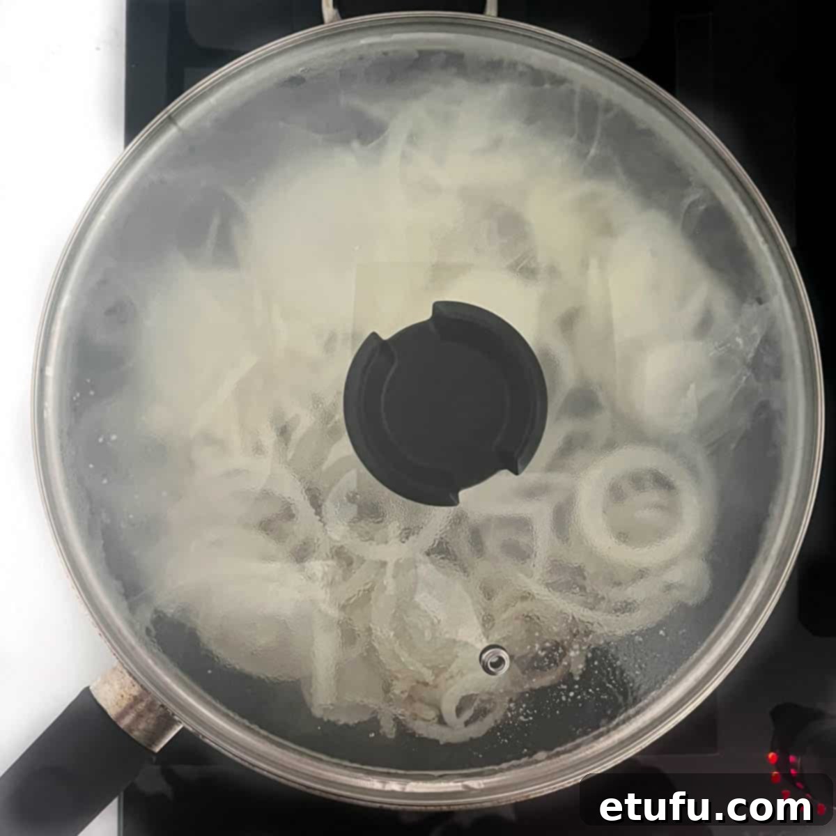 Thinly sliced onions gently frying in a pan with a lid on, a dollop of butter visible, beginning to soften for the Flammkuchen topping.