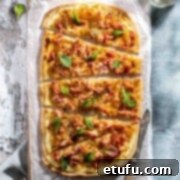 Flammkuchen, a traditional French-German pizza, freshly baked and sliced into wedges, resting on a rustic wooden table. The thin, crispy crust is visible, topped with caramelized onions, bacon lardons, and melted Gruyère cheese, garnished with fresh chives.