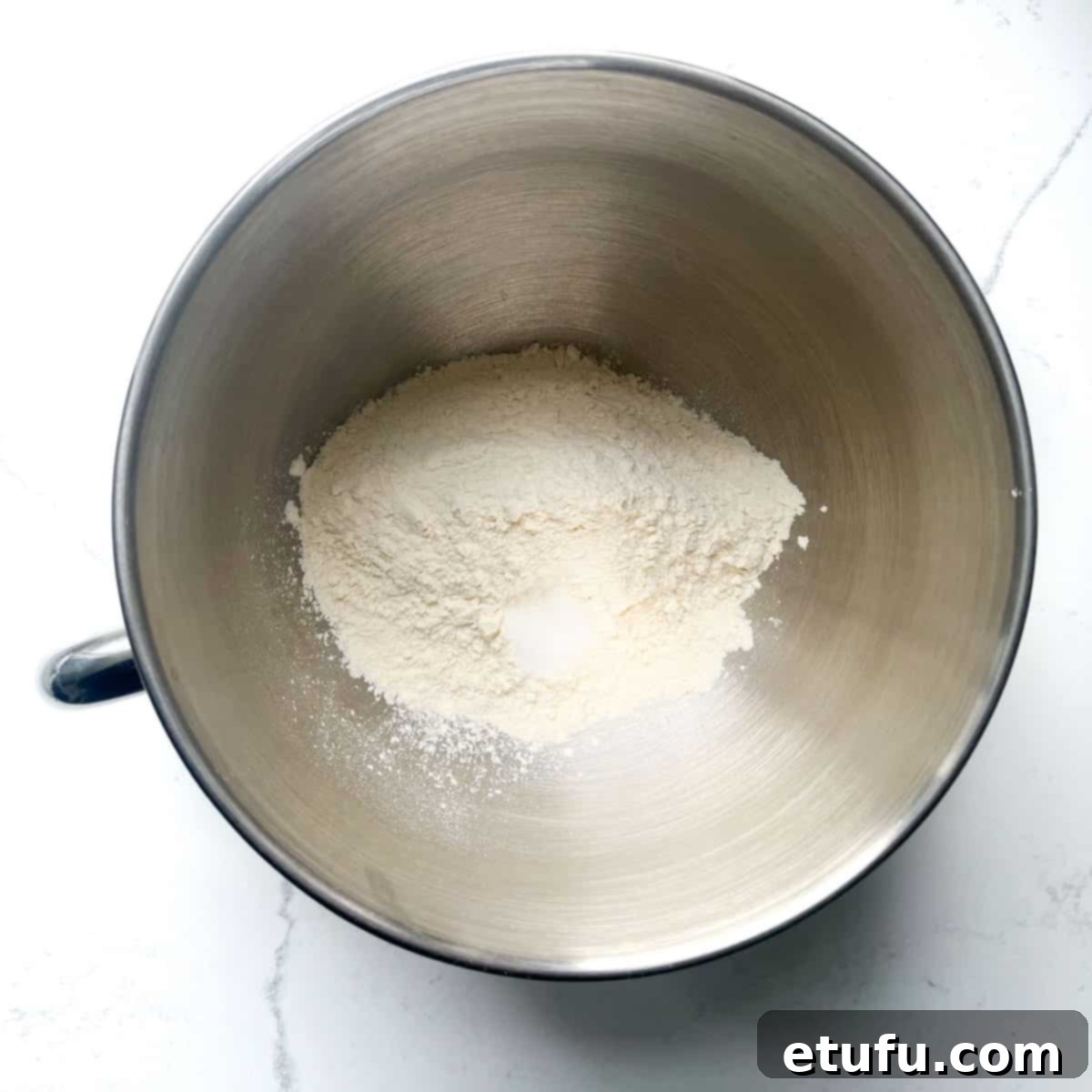 A large mixing bowl containing all-purpose flour and salt, ready to be combined for the Flammkuchen dough.