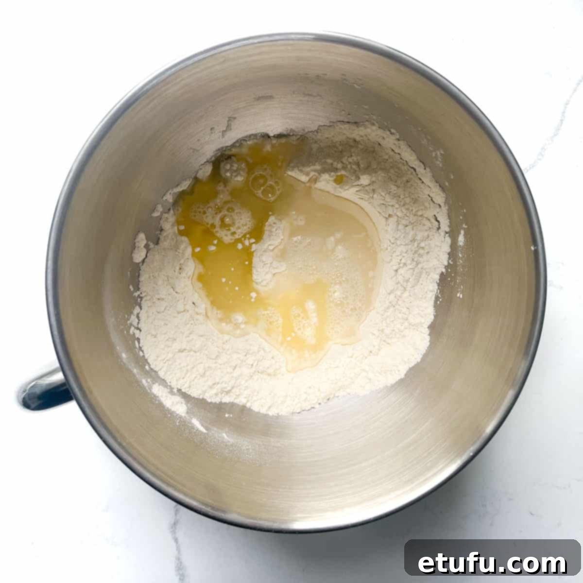 Warm water and olive oil being poured into a mixing bowl containing flour and salt, initiating the Flammkuchen dough preparation.