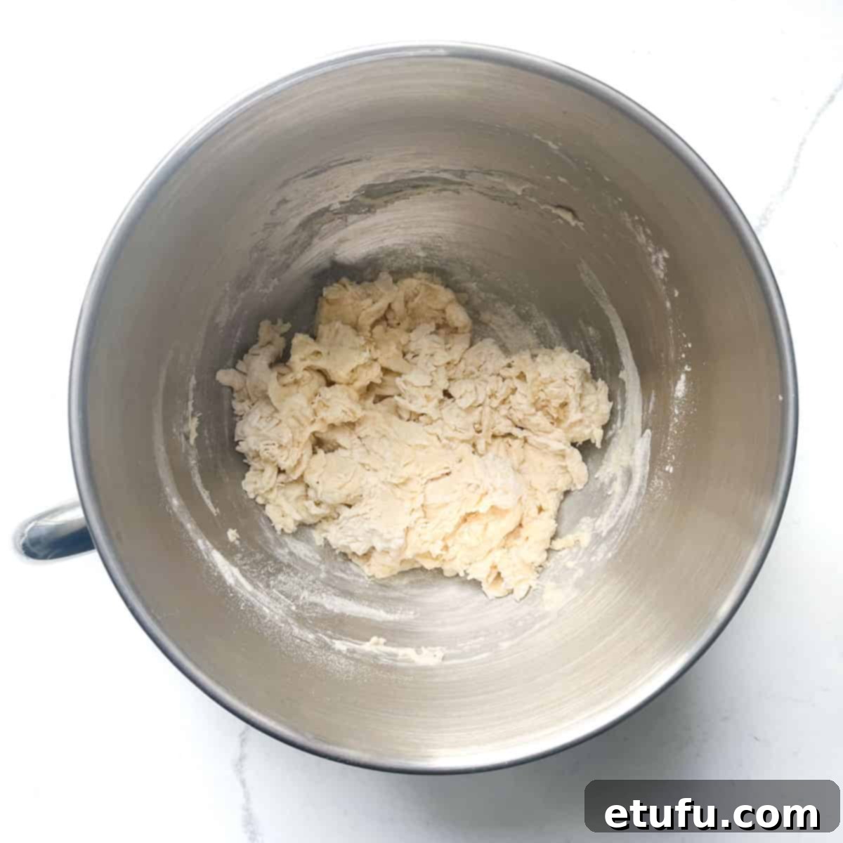 Flammkuchen dough ingredients, including flour, salt, water, and olive oil, loosely combined in a mixing bowl before kneading, showing a shaggy texture.
