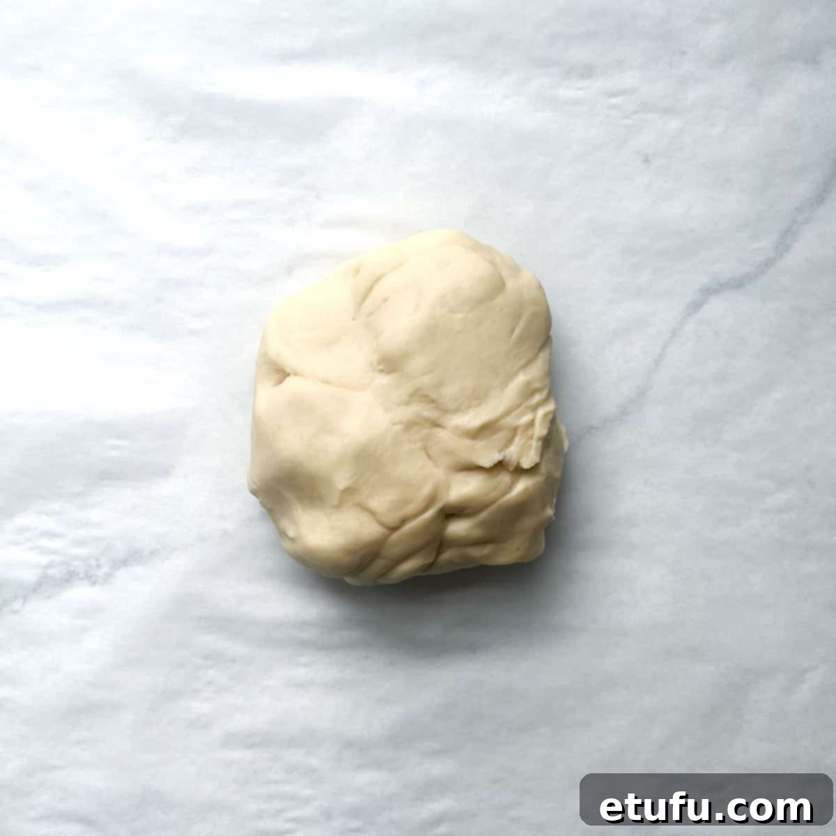 A smooth, round ball of Flammkuchen pizza dough placed centrally on a piece of parchment paper, ready for rolling.