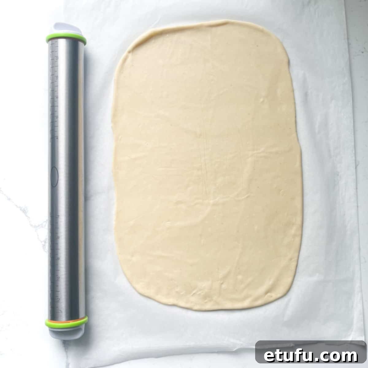 A Flammkuchen pizza base, rolled out thinly into an oblong shape on parchment paper, showcasing its readiness for toppings.