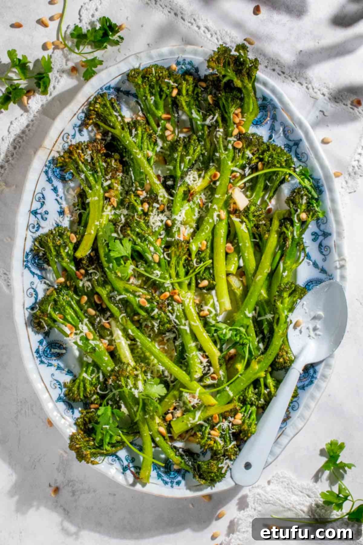 Roasted tenderstem broccoli on an oval plate with toasted pine nuts and parmesan, ready to serve.