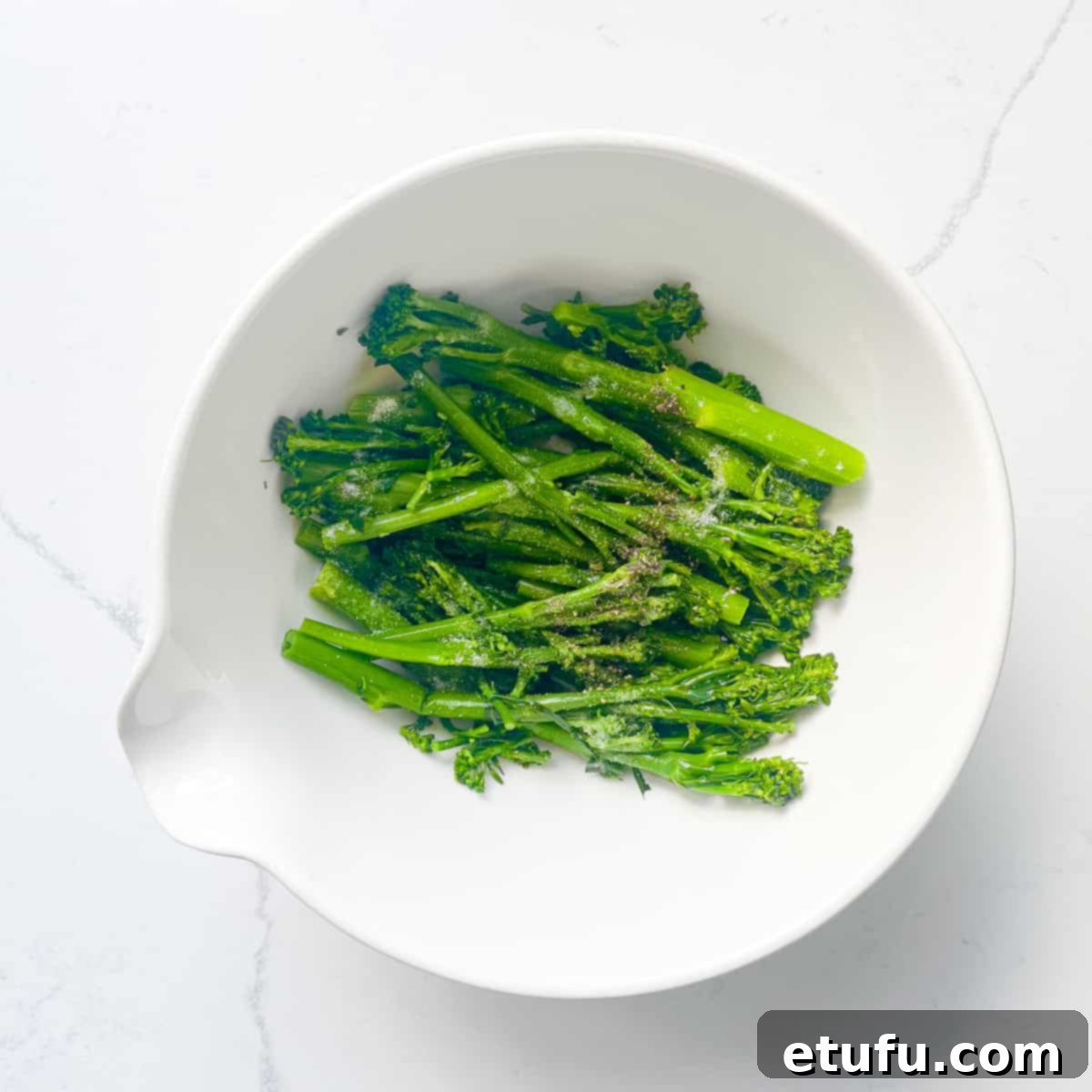 Tenderstem broccoli in a large white bowl, ready for seasoning.