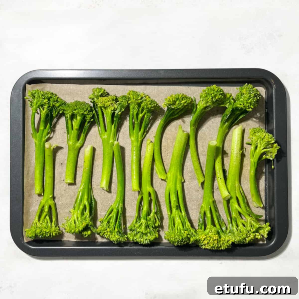 Tenderstem broccoli spread in a single layer on a baking sheet for even roasting.
