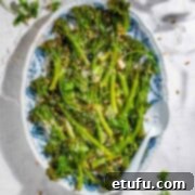 Roasted tenderstem broccoli on an oval plate with toasted pine nuts and parmesan.