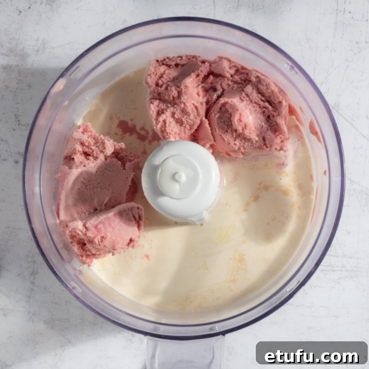 Adding all the ingredients for strawberry milkshake with ice cream in a blender.
