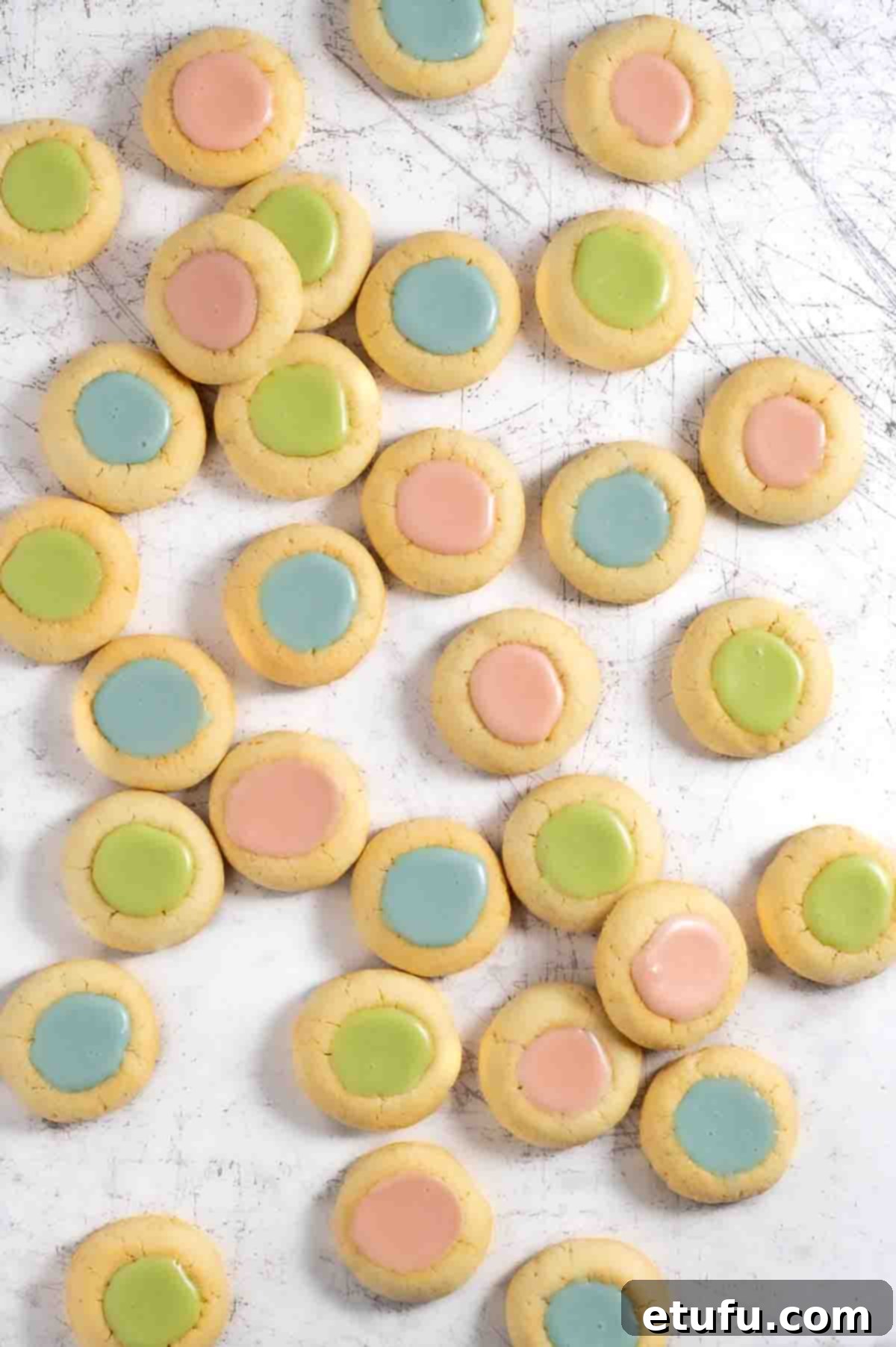 Pink, blue and green thumbprint icing cookies scattered across a white surface.