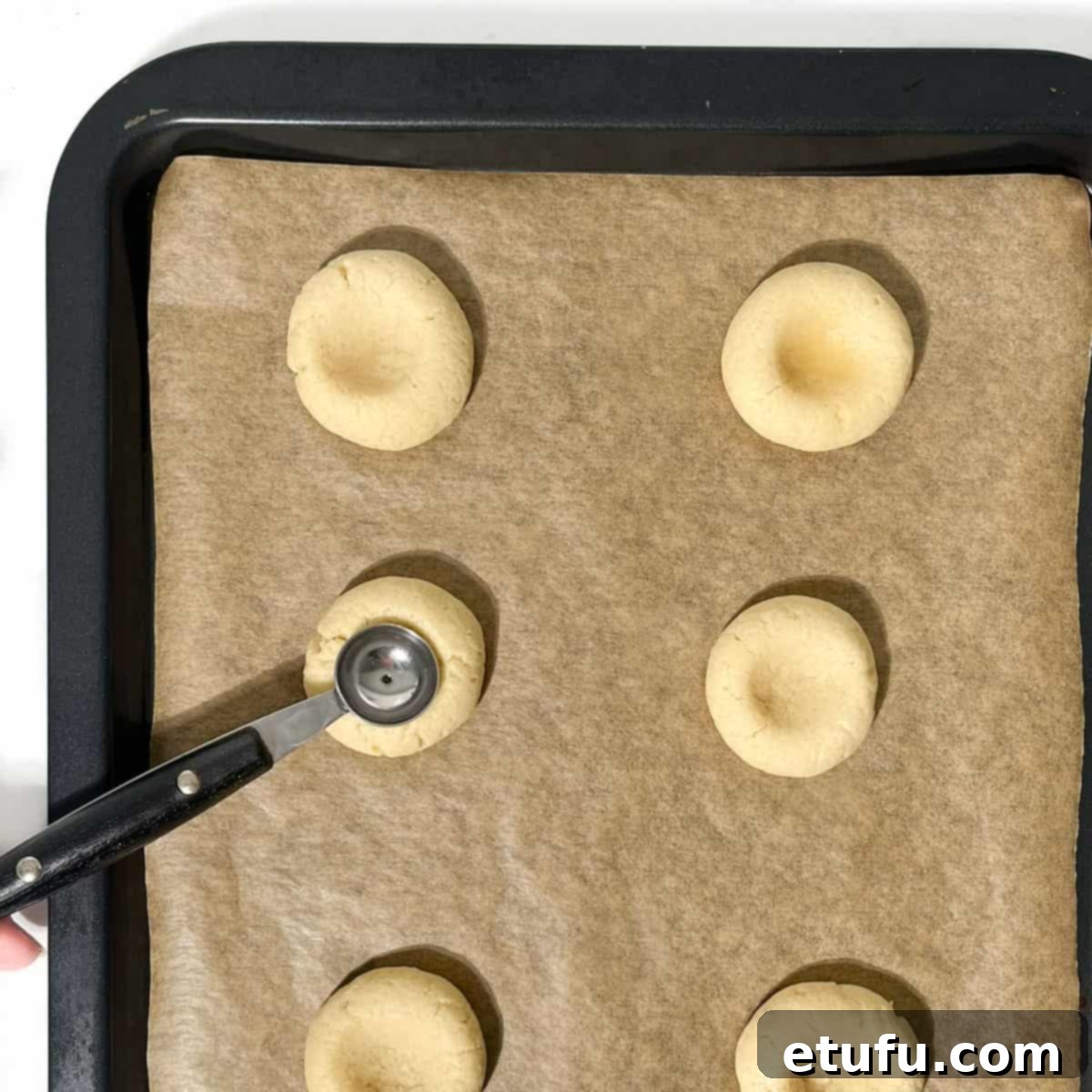 Indenting half-baked thumbprint cookies with a small melon baller on a baking tray.