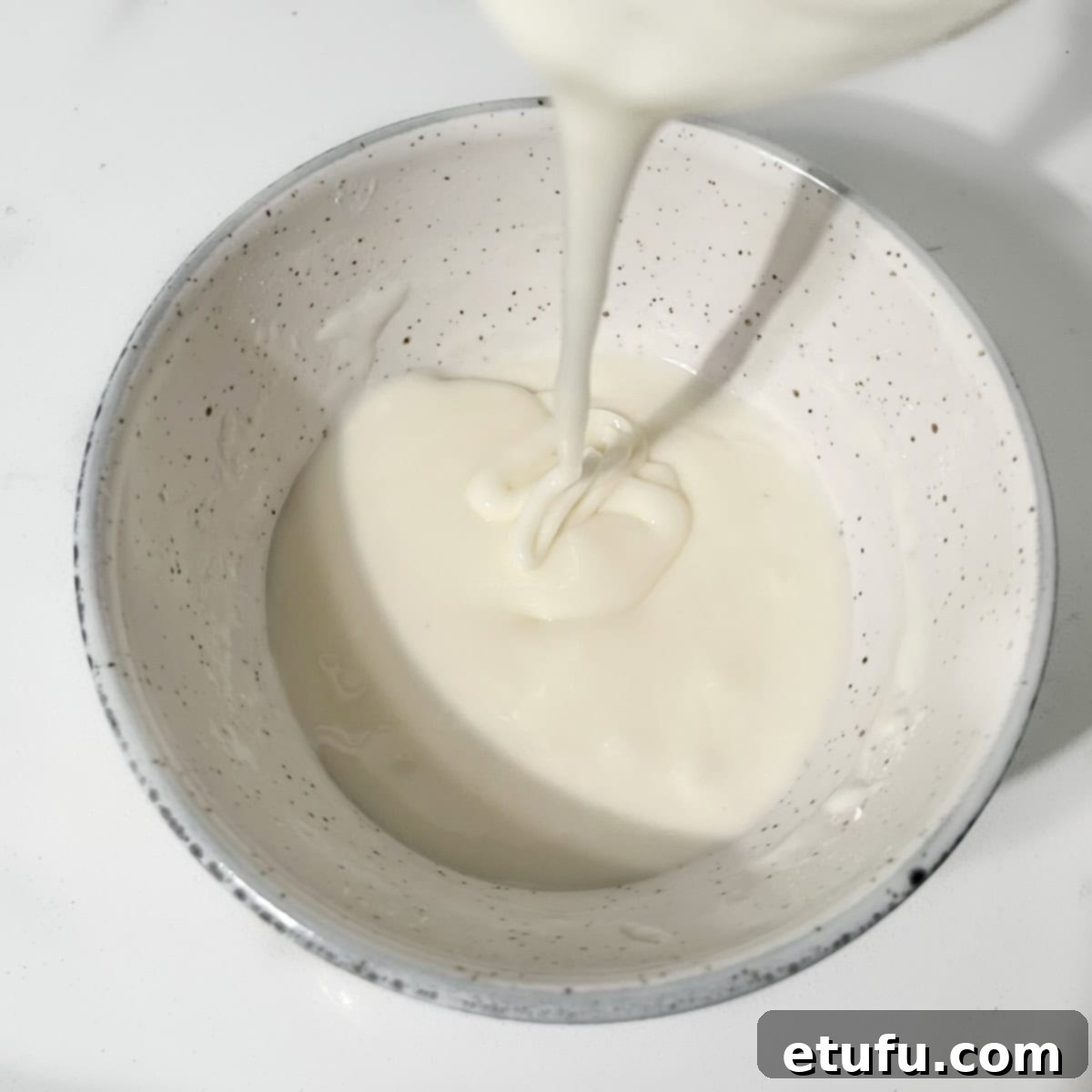 Demonstrating the consistency of the runny frosting for thumbprint cookies in a small white bowl.