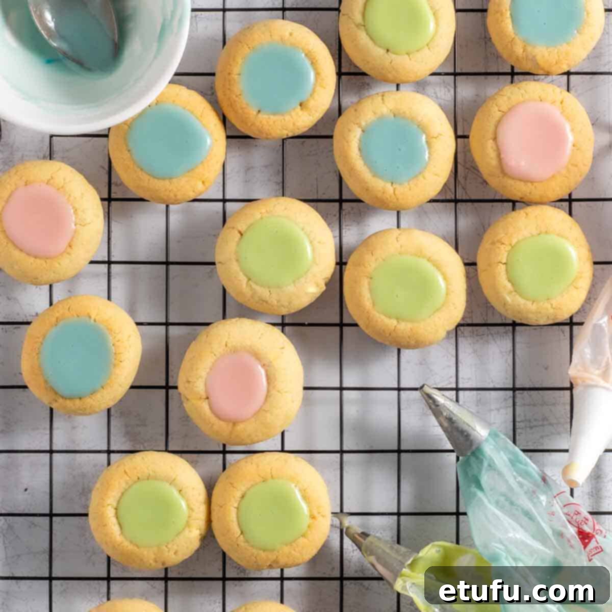 Thumbprint icing cookies on a wire cooling rack surrounded by piping bags.