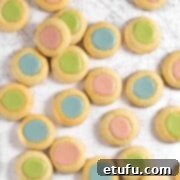 Pink, blue and green thumbprint icing cookies scattered across a white surface.
