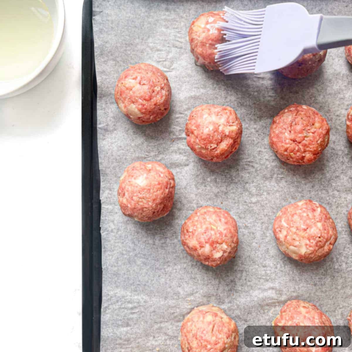 Meatballs being brushed with oil using a pastry brush.