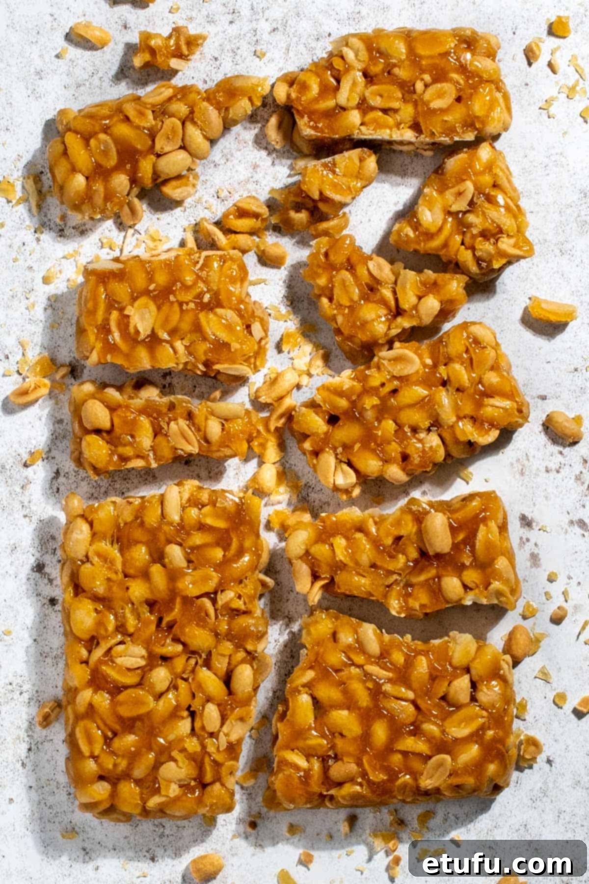 Irresistible homemade peanut brittle without corn syrup, expertly broken into rustic pieces and arranged enticingly on a pristine white background, showcasing its golden caramel and crunchy peanuts.