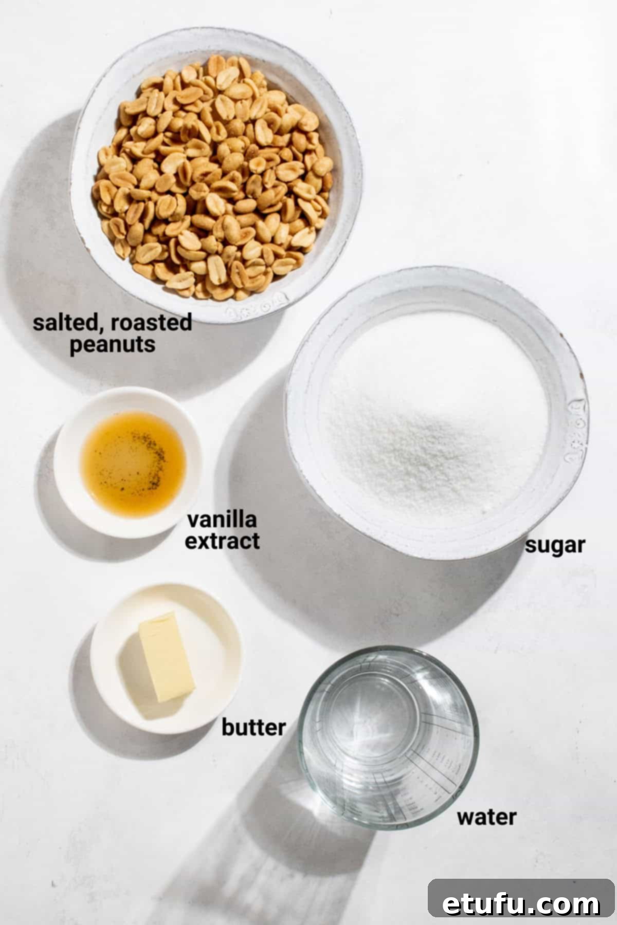 Five simple ingredients for making peanut brittle without corn syrup: granulated sugar, water, butter, vanilla extract, and roasted salted peanuts, neatly arranged for preparation.