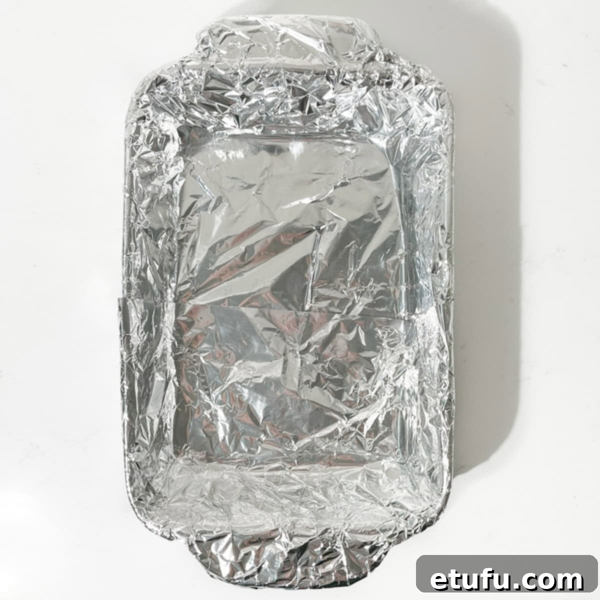 A baking dish precisely lined with aluminum foil and lightly oiled, ready to receive the hot peanut brittle mixture.