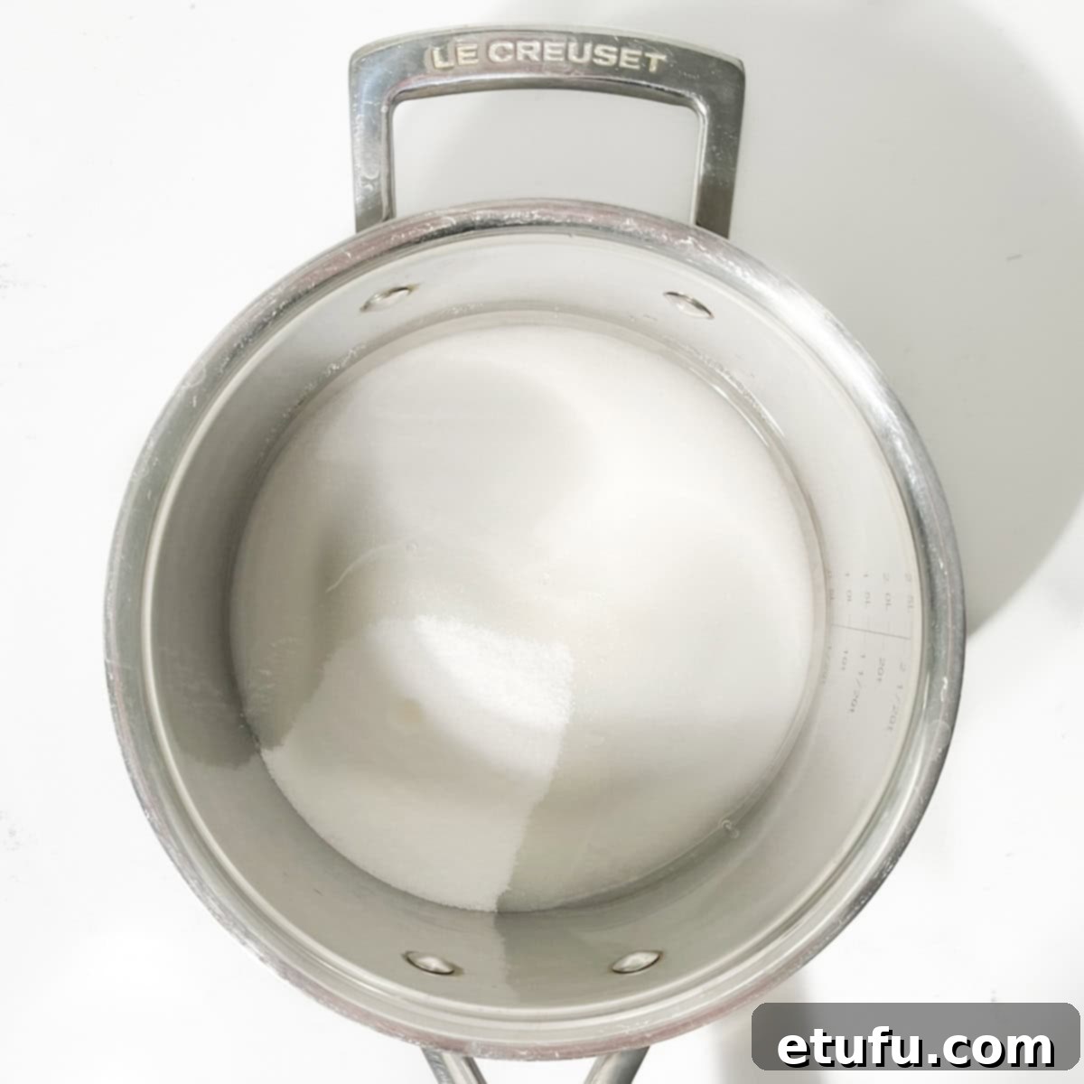 Granulated sugar and water combined in a large, heavy-bottomed saucepan, ready to be heated for the peanut brittle.