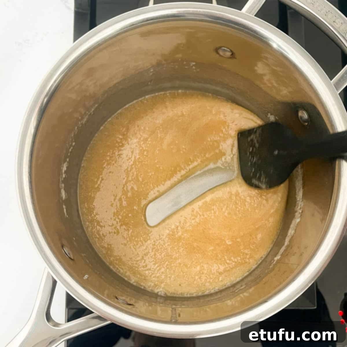 A spatula tracing a clear, thick line through the caramelizing sugar mixture in a saucepan, indicating it has reached the hard-crack stage for peanut brittle.