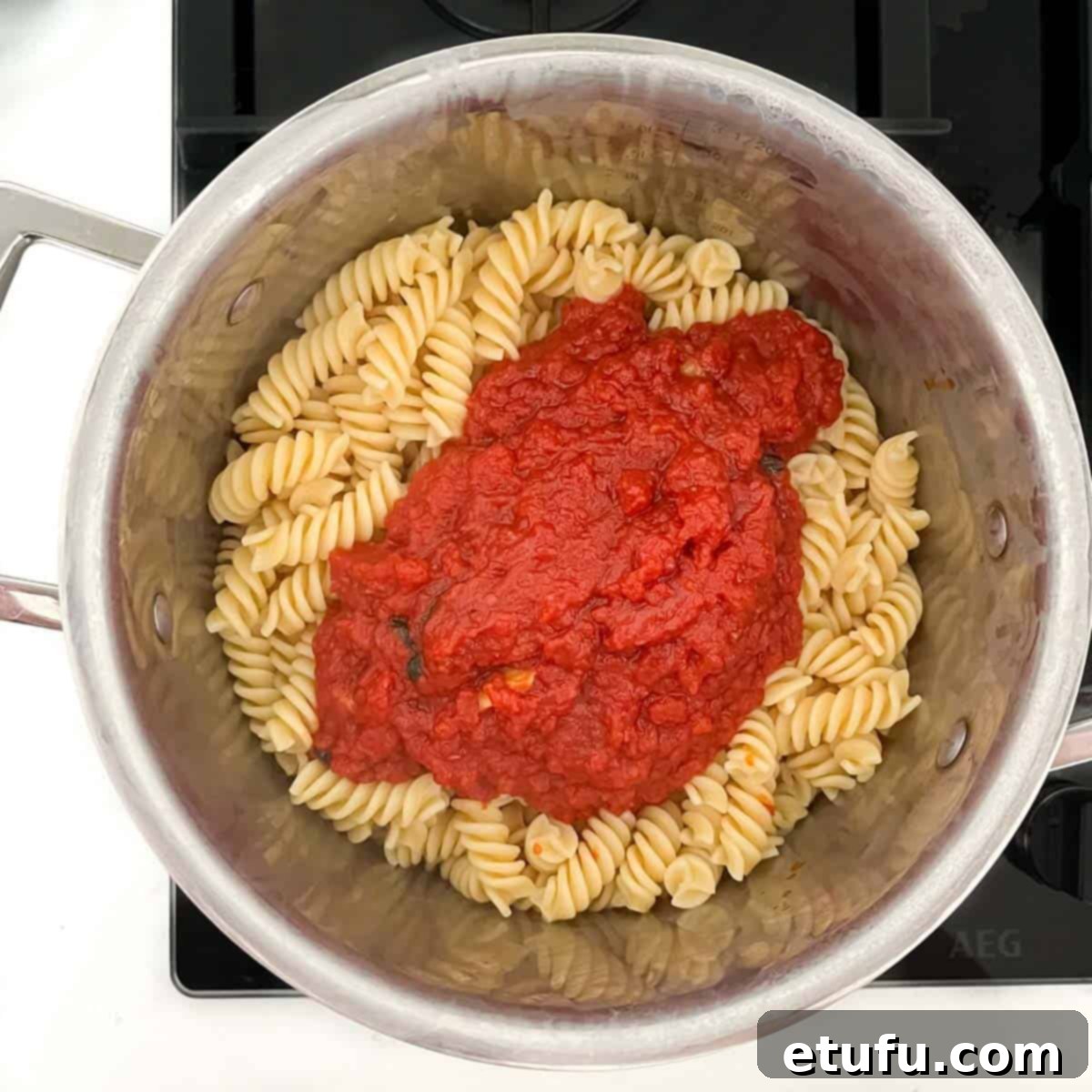 Tomato sauce added to a pan of cooked pasta.