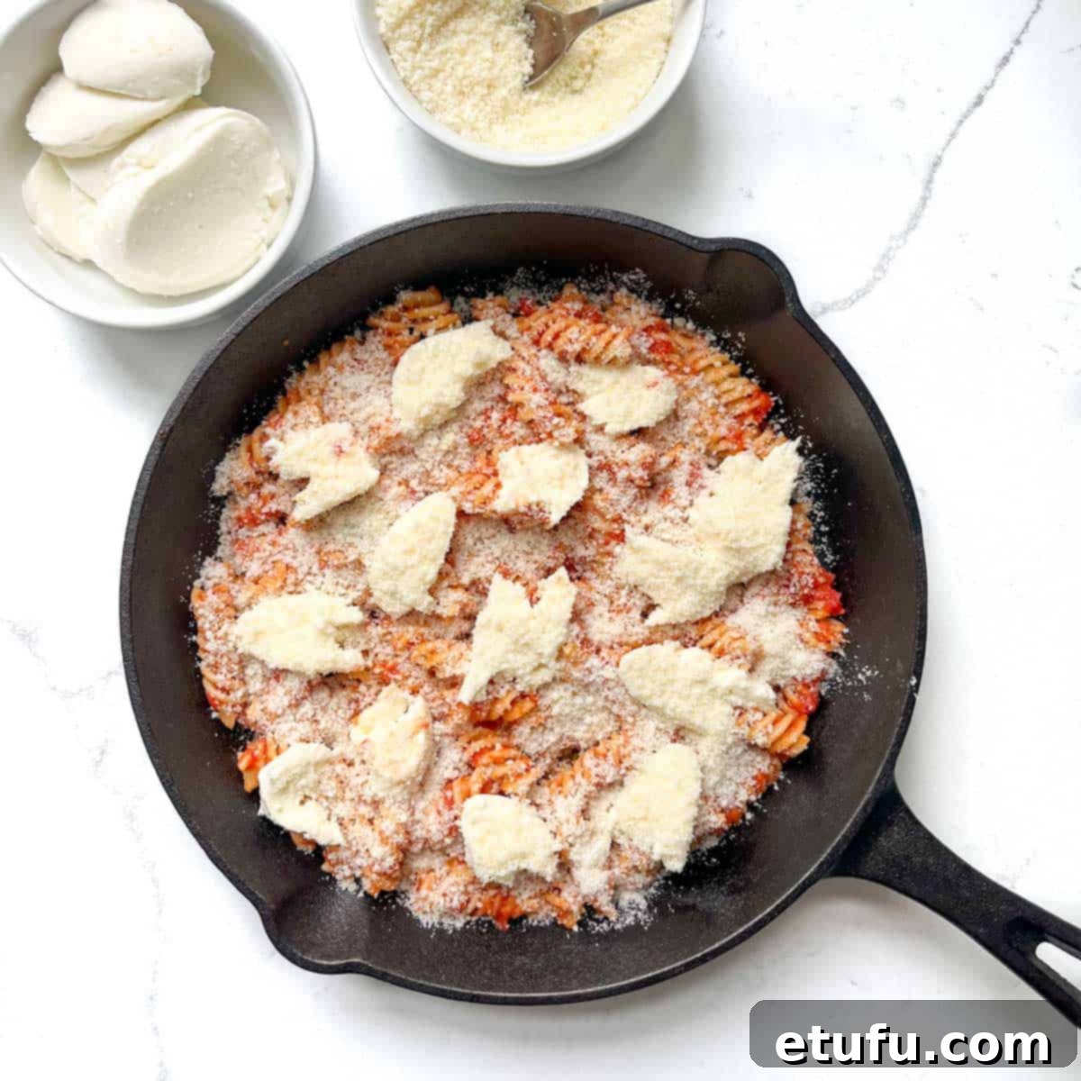 The first layer of parmesan added to the first layer of pasta in a black cast iron pan.