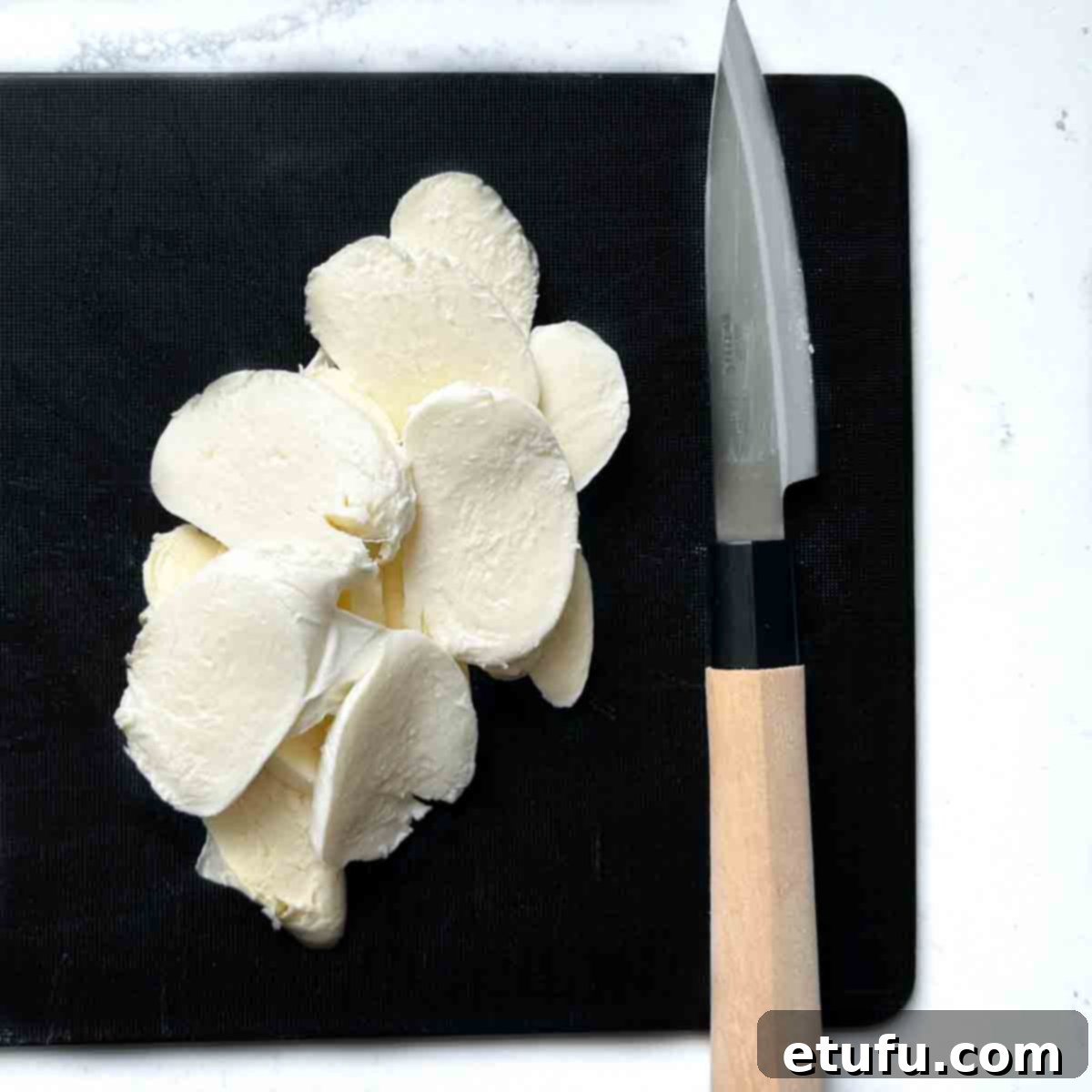 Mozzarella slices on a black chopping board.