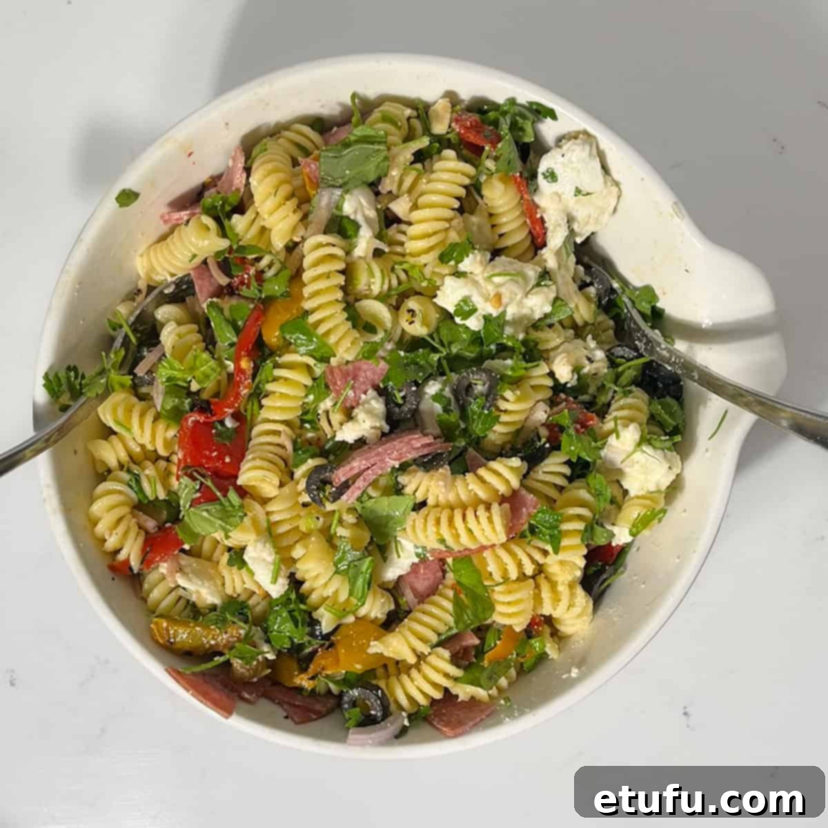 Mixing the summer pasta salad with the cooked pasta in a large white bowl.