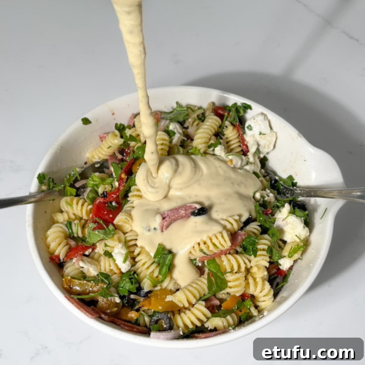 Adding the salad dressing to the cold pastas salad in a large white bowl.