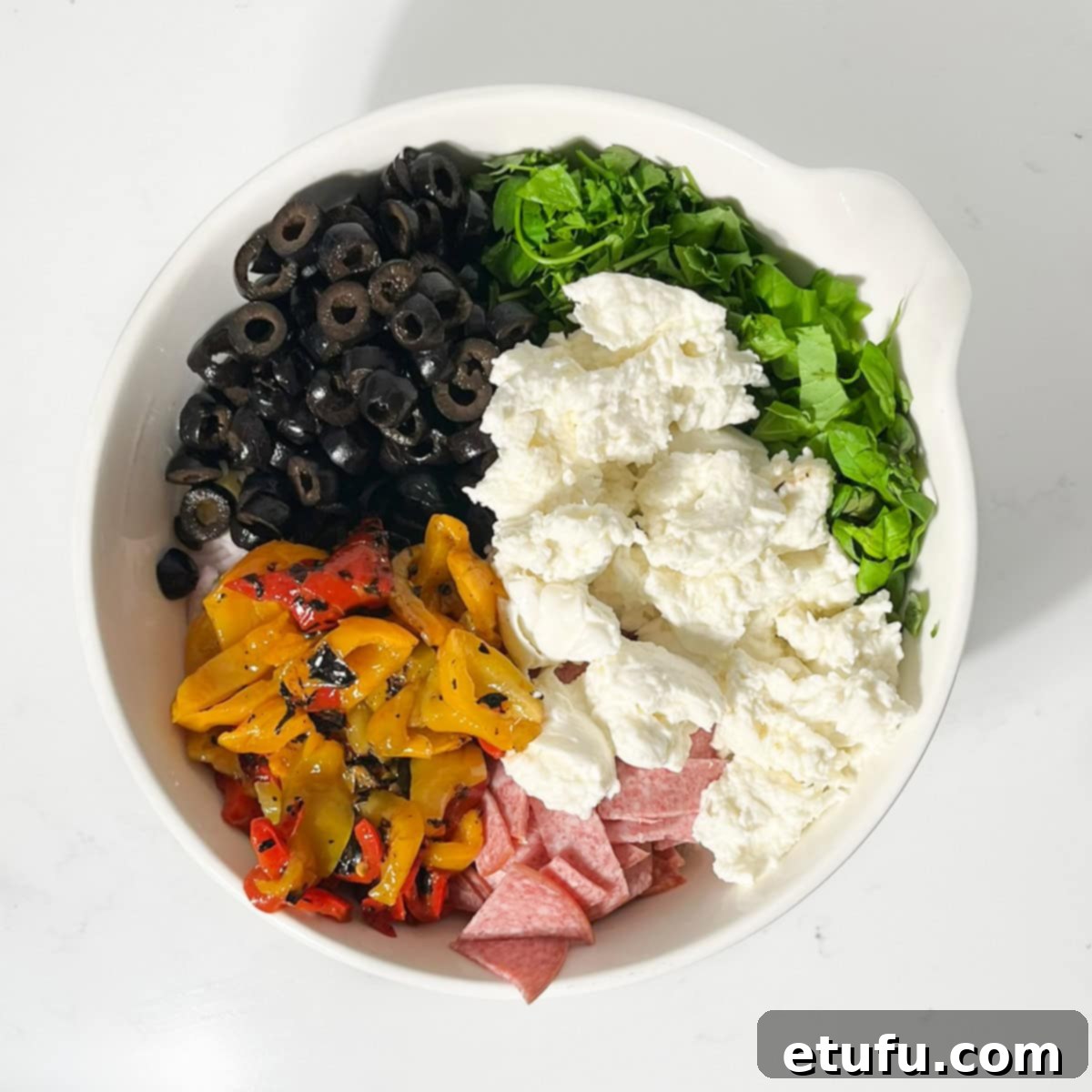 Adding all the salad-add-ins for the creamy italian pasta salad to the pasta in a large white bowl.
