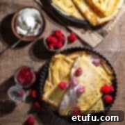 Pandekager folded in triangles in a black, round backing dish, served with raspberries, icing sugar, jam and cream.