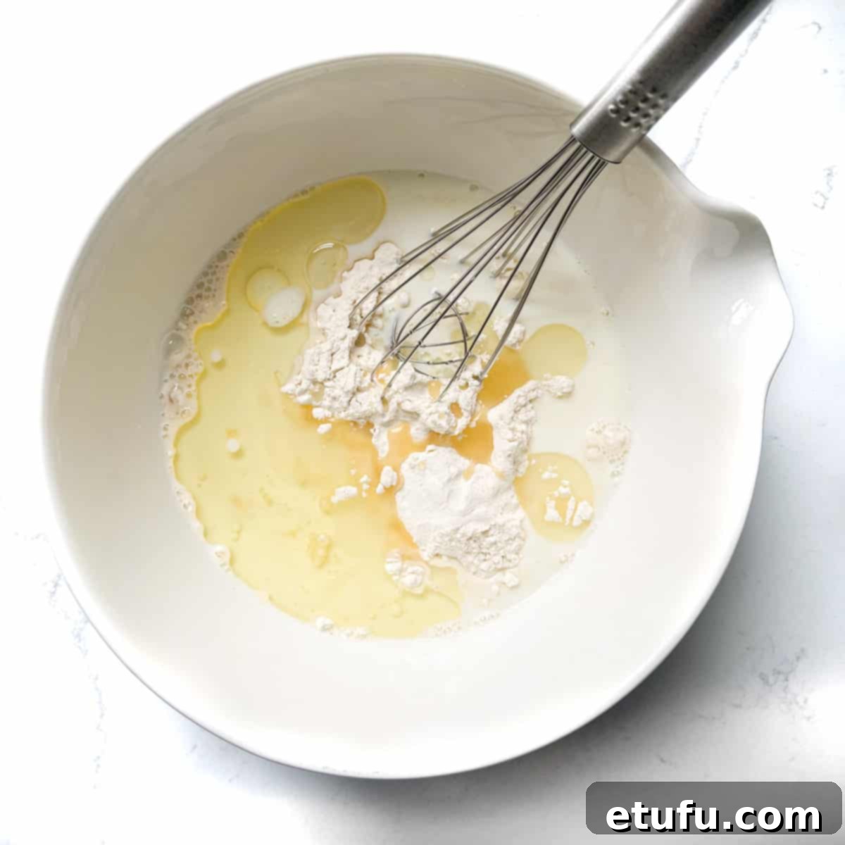 Adding half the milk and oil to the dry ingredients in a large white bowl.