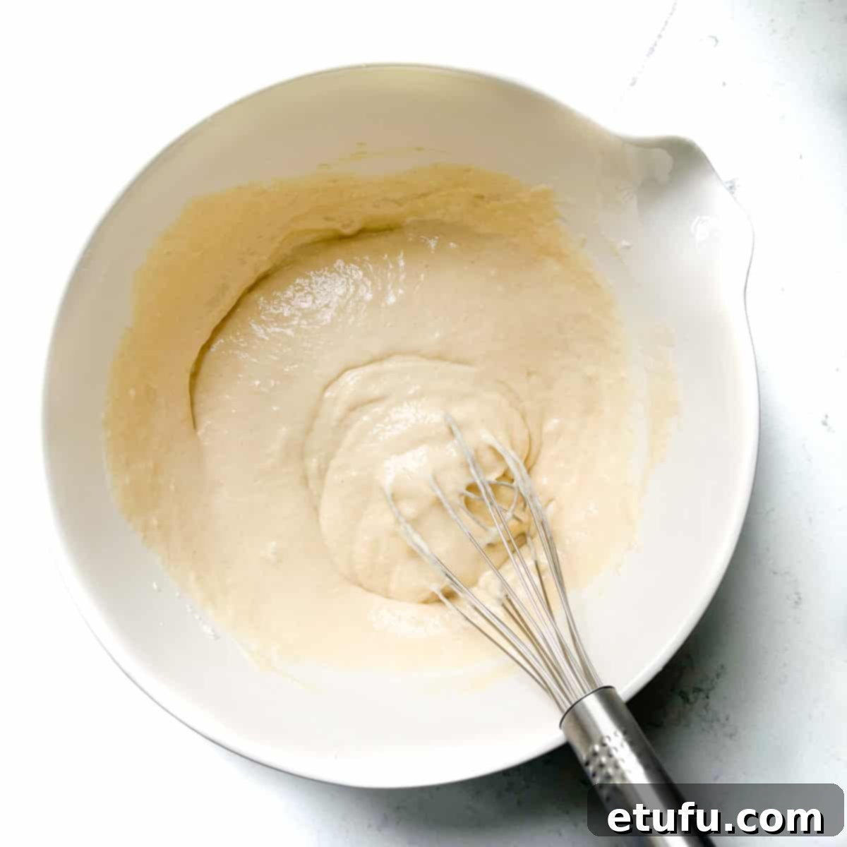 Mixing the dry ingredients with half the milk and oil in a large white bowl.